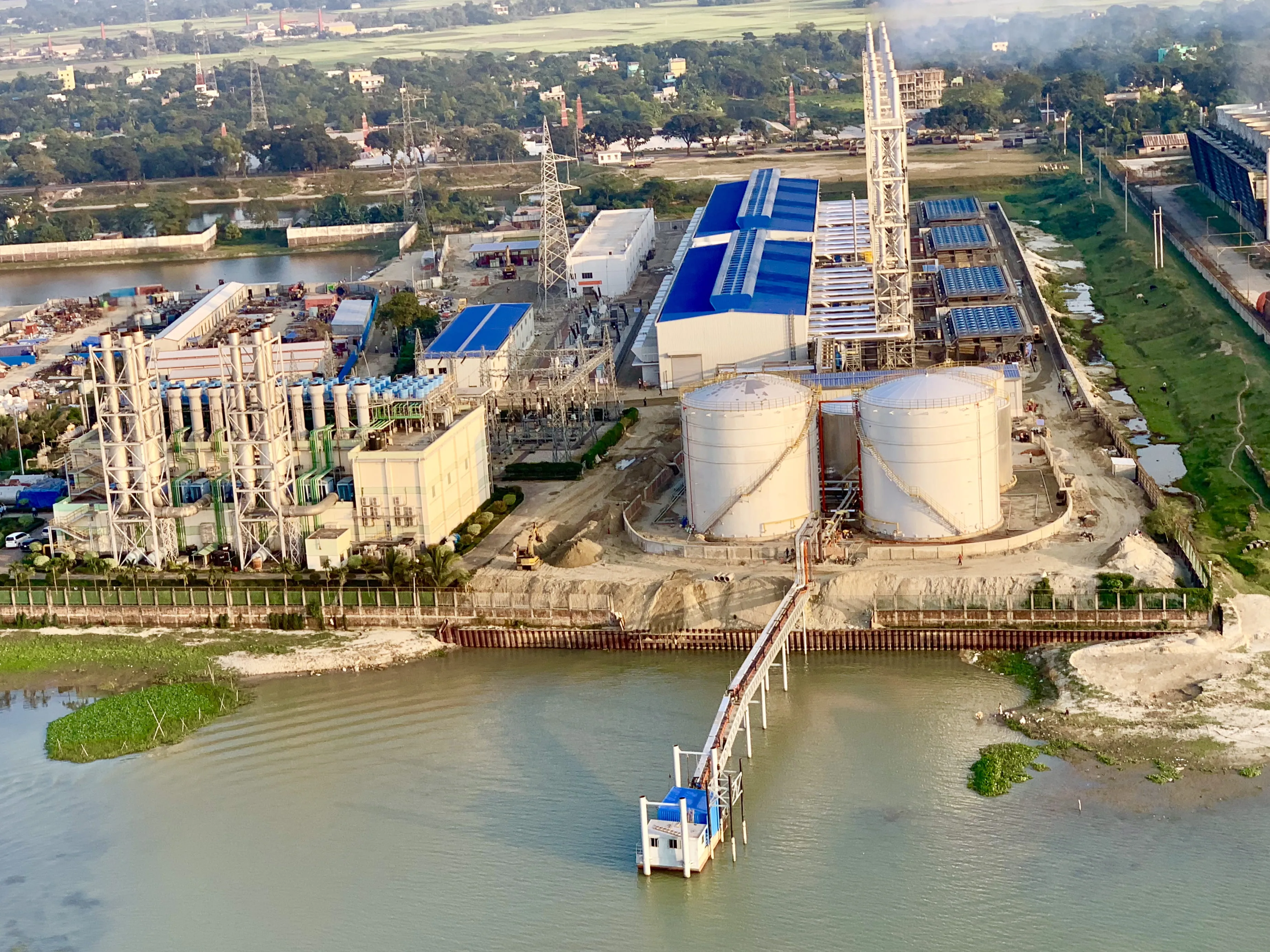 Industrial power plant facility with water intake and storage tanks beside a river